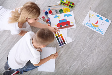 Mother with cute boy painting picture on sheet of paper, indoors