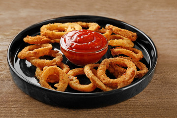Fototapeta premium Plate with fried onion rings and sauce on wooden table