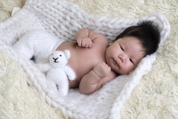 Portrait of Asia boy newborn is lay down on white fur background with bear .