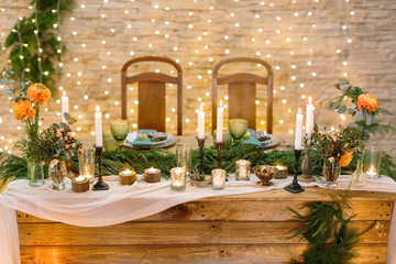 romance, comfort, holidays concept. romantic table setting for two lovers with numerous of the candles in various candle holders, it also decorated with little bunches and lights on the background