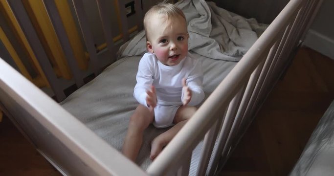 Adorable baby laughing and clapping hands. Toddler claps his hands clapping sitting in a cot baby crib