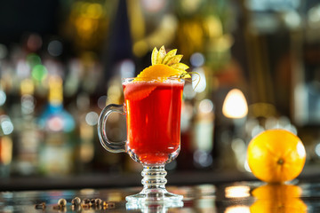 Closeup glass of red cocktail decorated with orange and apple slices at bright bar counter background.
