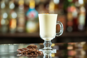 Glass of milk cocktail decorated with chocolate at bar counter background.