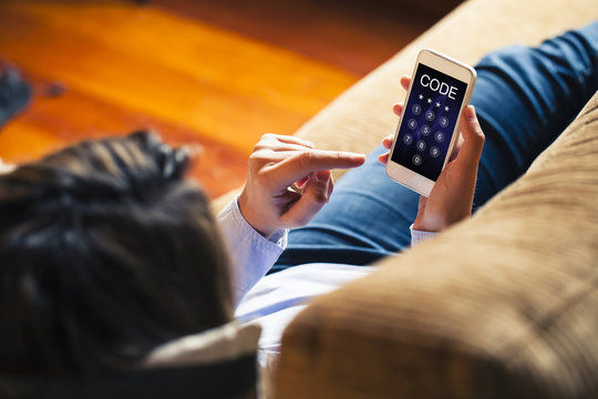 Woman entering unlocking code in a mobile phone while lies down on a sofa at home.