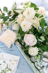 marriage, sentiment, proposal concept. wonderful bridal bouquet of elegant creamy and pink roses decorated with small blue flowers placed on the silver shining tray nearby with pillows for rings