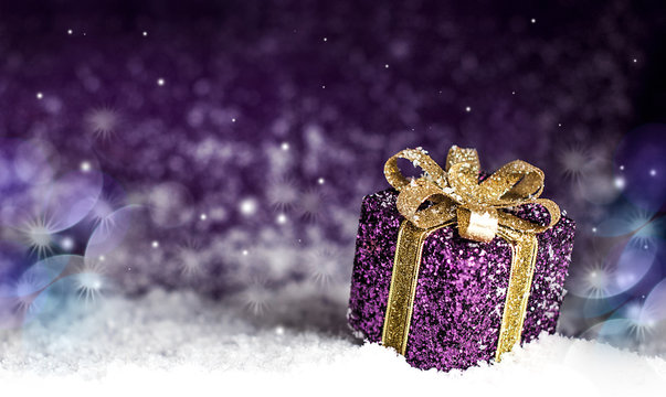 purple shiny gift with a gold bow, on a snowy background