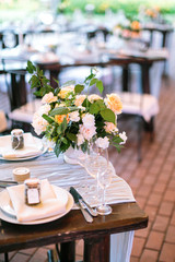 food, culture, decorating concept. bunch made of perfect beautiful roses in different colours placed on the table of garden restaurant nearby with served for celebration plates and cutlery