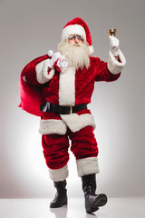 santa claus holding presents bag on shoulder and rings bell