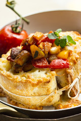 Gratiniertes Baguette mit Ratatouille in einer Pfanne mit einer Ofentomate im Hintergrund