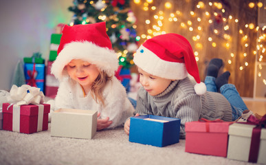 Fototapeta na wymiar Boy and girl lying on the floor with presents near christmas tree