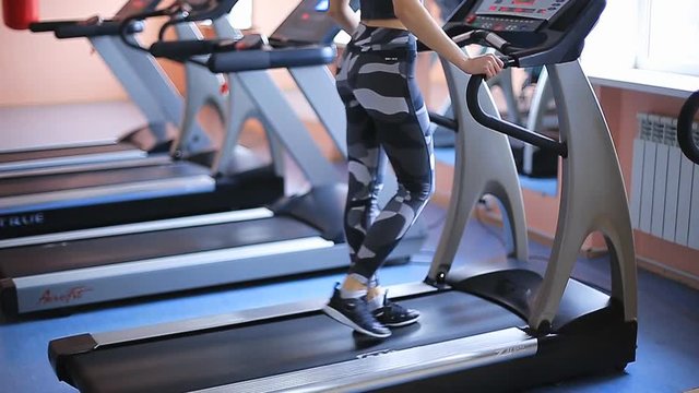 The beautiful girl is engaged in the gym. Back view of female legs walking and running on treadmill in gym, woman training