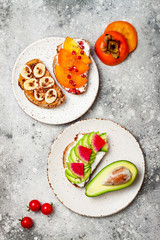 Healthy breakfast toasts with peanut butter, banana, chocolate granola, avocado, watermelon radish, persimmon, pomegranate, chia seeds. Top view, flat lay