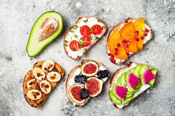 Healthy breakfast toasts with peanut butter, banana, chocolate granola, avocado, watermelon radish, persimmon, pomegranate, chia seeds, tomato, figs, blackberry.