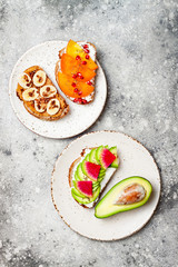 Healthy breakfast toasts with peanut butter, banana, chocolate granola, avocado, watermelon radish, persimmon, pomegranate, chia seeds. Top view, copy space