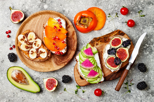 Healthy breakfast toasts with peanut butter, banana, chocolate granola, cream cheese, figs, blackberry, persimmon, pomegranate, chia seeds, avocado. Top view, overhead