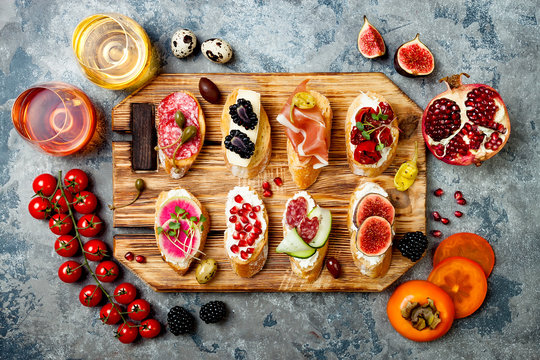 Appetizers table with italian antipasti snacks and wine. Brushetta or authentic traditional spanish tapas set on wooden rustic board over grey concrete background. Top view, flat lay