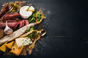 Assortment of cheeses and traditional sausages on a wooden background. Brie cheese, blue cheese, gorgonzola, fuete, salami. Free space for text. Top view.