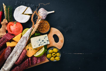 Assortment of cheeses and traditional sausages on a wooden background. Brie cheese, blue cheese, gorgonzola, fuete, salami. Free space for text. Top view.