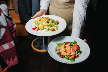 Tasty slice of fried salmon served with mix salad of kale leaves, cherry tomatoes and bocconcini cut in halves, cucumber, served on a white plate. Healthy food. Selective focus