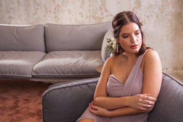 Entspannte junge Frau sitzt im festlichen Kleid zuhause im Sessel