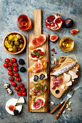 Appetizers table with italian antipasti snacks and wine in glasses. Brushetta or authentic traditional spanish tapas set, cheese variety board over grey concrete background. Top view, flat lay - obrazy, fototapety, plakaty