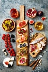 Fototapeten Appetizers table with italian antipasti snacks and wine in glasses. Brushetta or authentic traditional spanish tapas set, cheese variety board over grey concrete background. Top view, flat lay © sveta_zarzamora