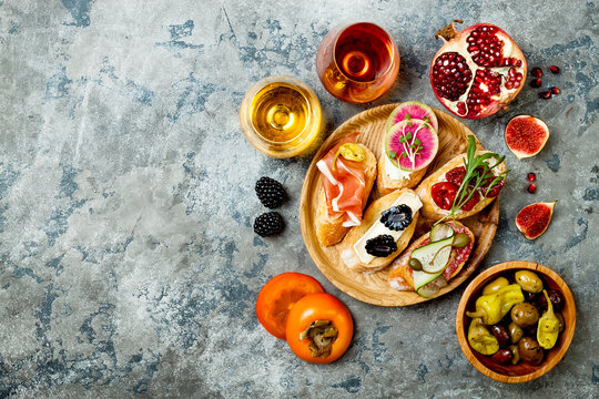 Appetizers table with italian antipasti snacks, wine in glasses. Brushetta or authentic traditional spanish tapas set, cheese variety board over grey concrete background. Top view,  copy space