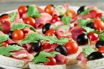 Close up of a plate of delicious tasty ham canapes with cherry tomatoes and black olives decorated with fresh rucola leaves greens healthy delicious organic food eating gourmet concept.