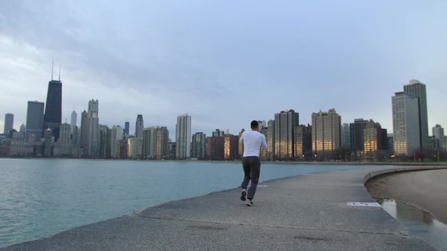 Man is running on thr ebankment. Athlete training outdoors. Downtown with skyscrapers on the background. Morning sunrise.