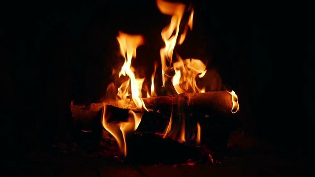Logs burning in dark room in open fireplace in slow motion 96fps. Closeup on slowly burning logs in open indor fireplace.