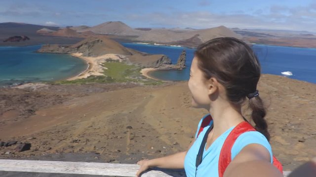 Galapagos tourist selfie video on Bartolome Island. Travel vacation adventure woman taking selfie self portrait video at famous viewpoint and visitor site of iconic landscape with Pinnacle Rock.