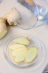 Slices of ginger root on glass plate over wooden board.