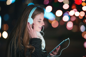 Woman with headphones using tablet and listening music in city at night