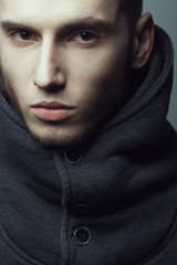 Male beauty concept. Portrait of brutal young man with short hair wearing gray sweatshirt with high collar and buttons posing over gray background. Modern street style. Close up