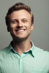 Obraz premium Male beauty, boy next door concept. Portrait of smiling 30-year-old man standing over gray background. Close up. Classic style. Wavy glossy blond hair. Text space. Studio shot