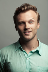 Male beauty, demon inside. Portrait of smiling 30-year-old man standing over gray background. Close up. Classic style. Wavy glossy blond hair. Studio shot