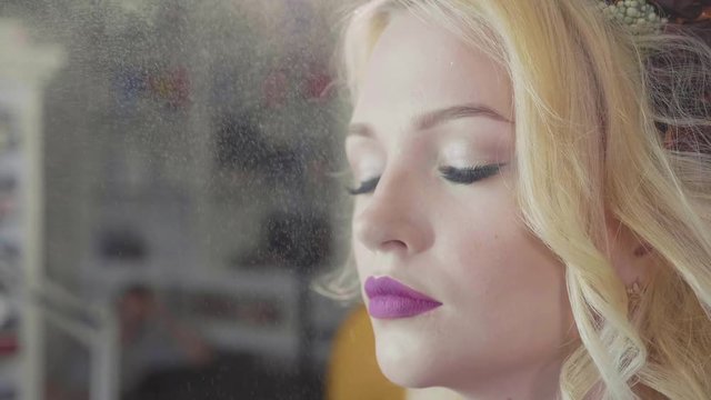 Moisturizing spray sprinkles on the face of the girl after makeup procedure