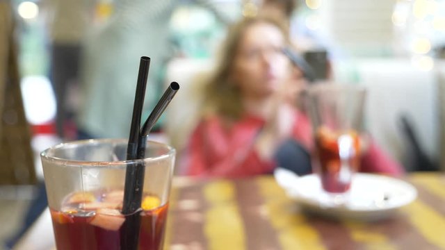 beautiful woman is resting in a cafe, drinking hot mulled wine and looking into her smartphone. 4k, background blur.