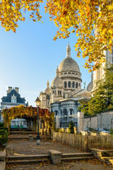 Rear view of the Basilica of the Sacred Heart of Paris in autumn at sunrise seen from a public park with orange leaves in the foreground against blue sky. - obrazy, fototapety, plakaty