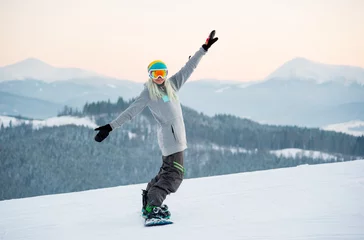 Fototapete Wintersport Aufnahme einer fröhlichen Snowboarderin, die sich beim Reiten in den Bergen amüsiert und auf der Piste posiert