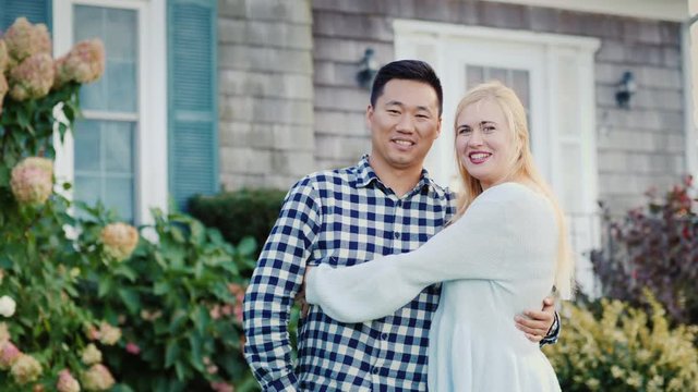 Portrait of a happy family on the threshold of their house. Asian man and Caucasian woman hugging, smiling and looking at camera