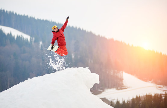 Male snowboarder jumping on the top of the snowy hill with snowboard, smiling to the camera. Skiing and snowboarding concept