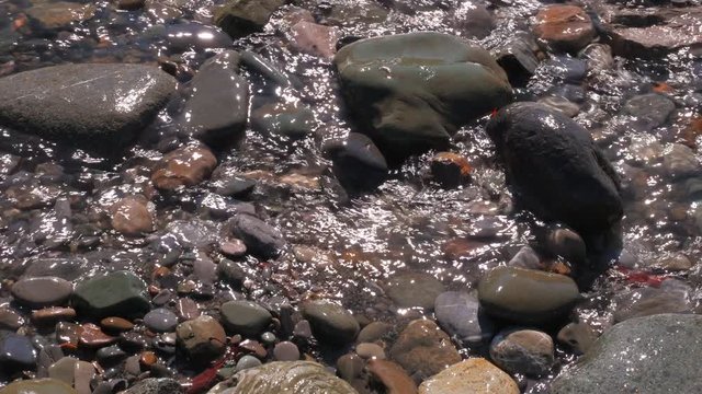Close up of fast water stream flowing around big and small stones. 4K. Panning shot