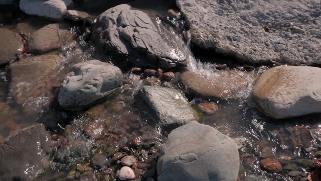 Panning shot of fast water stream flowing between big and small rocks and red leaves in autumn. 4K. Close up