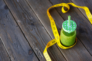 Detox green smoothie and measuring tape on wooden table for dieting and healthy fitness nutrition concept.