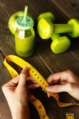 Healthy green detox, apple and dumbbells for slimming down. Woman with measuring tape before drinking fruit and vegetables smoothie for weight loss. Dieting and fitness nutrition concept.
