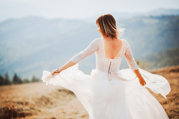 Wind blows bride's hair and dress while she poses on the mountain hill