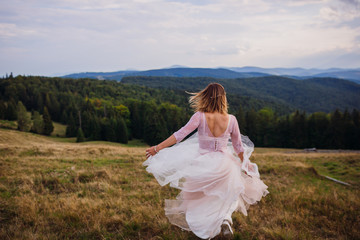 Fototapeta na wymiar Gorgeous bride whirls on the hill before beautiful mountain landscape