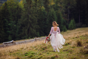 Bride runs along the hill with red wedding bouquet