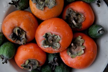 On the table, a fresh persimmon and feijoa on a platter